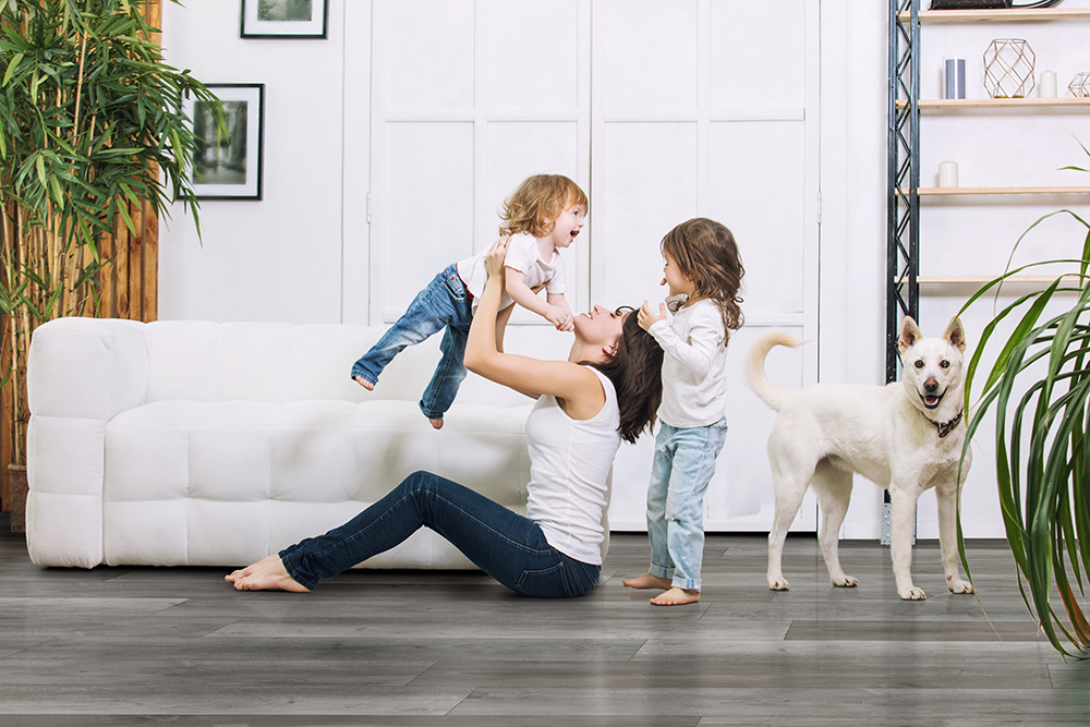 Family in a living room with durable LVT flooring that shows how LVT wear layer thickness can withstand kids and pets.