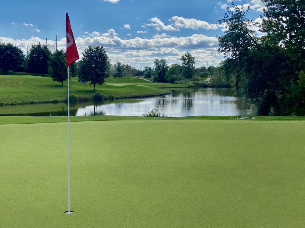 Commercial artificial turf putting green by a pond, showing a uniform low maintenance surface for golf courses.