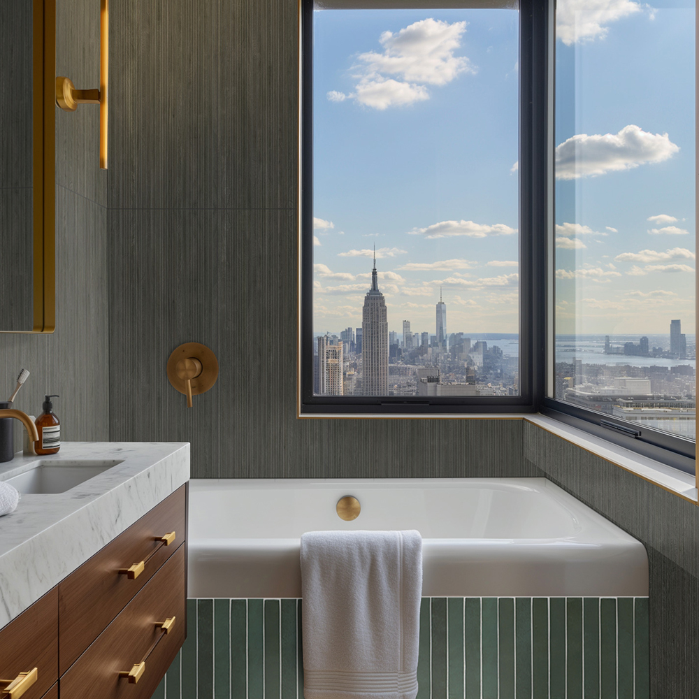 Modern bathroom featuring dark green fluted wall tiles around a bathtub, brass fittings and huge windows.