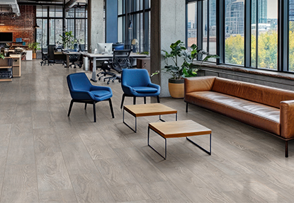 Modern office space with gray wood look commercial tile flooring, leather sofa, and blue lounge chairs